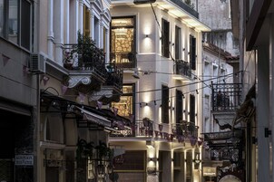 A narrow street with multi-story buildings, balconies with plants, and string lights.