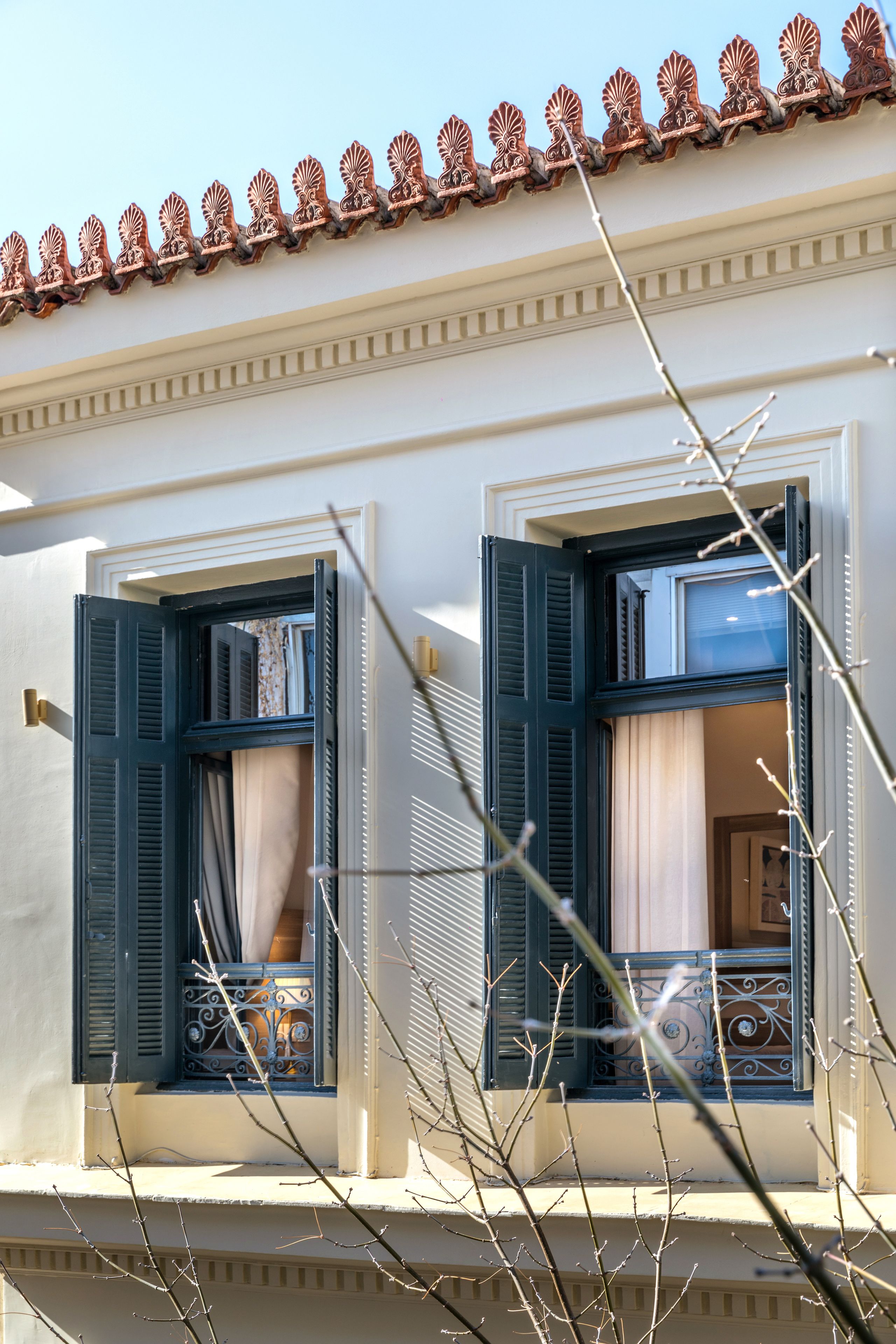 A building with two windows, each with blue shutters and decorative iron grilles.