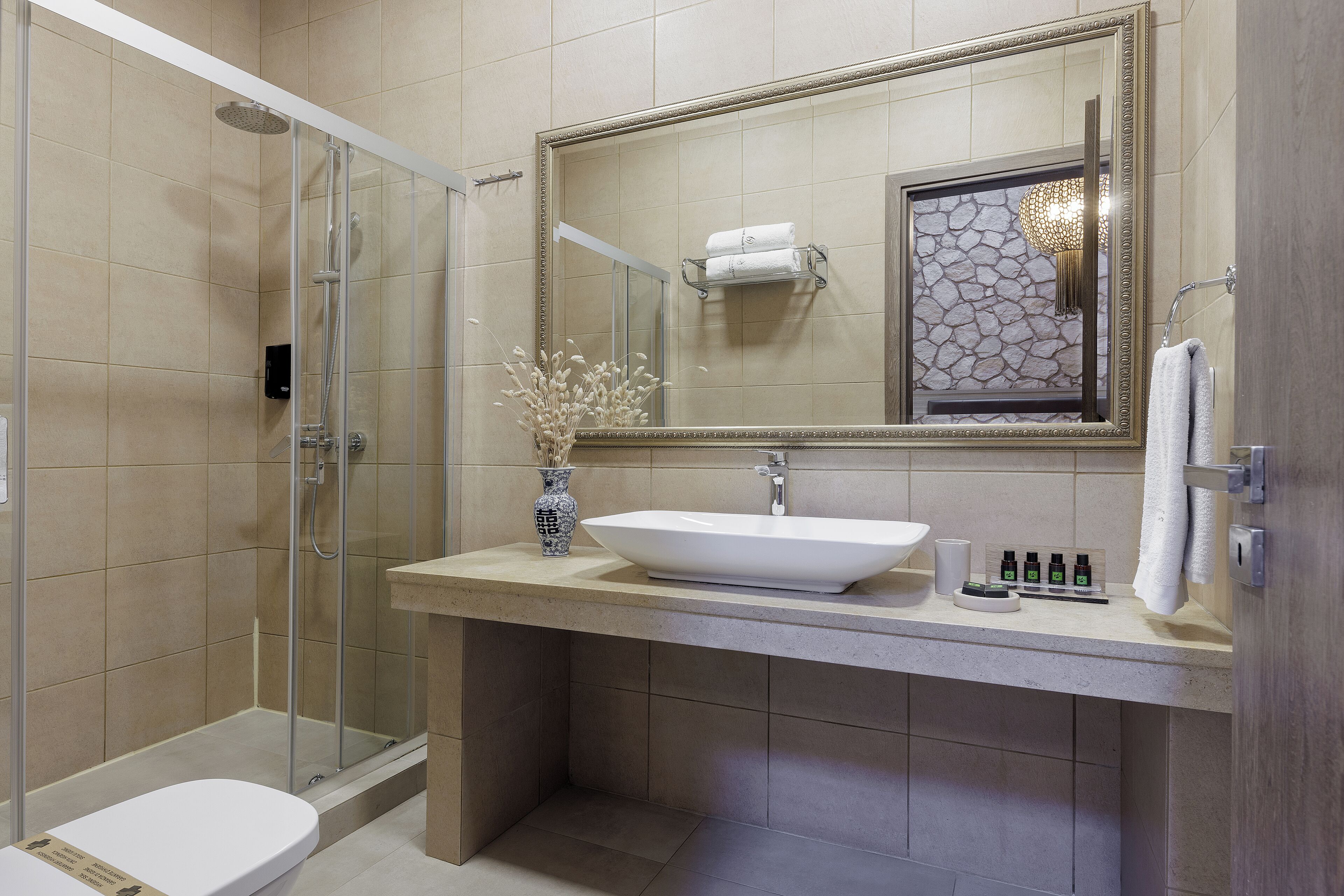 A modern bathroom with a glass-enclosed shower, a large mirror, a beige sink, and a white toilet.