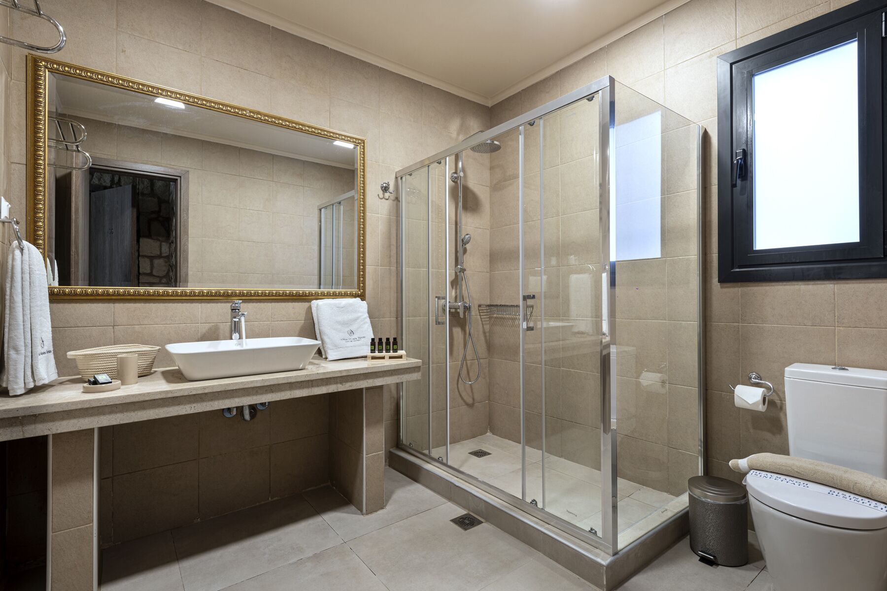 A modern bathroom with a large mirror, a glass-enclosed shower, a sink, and a toilet.