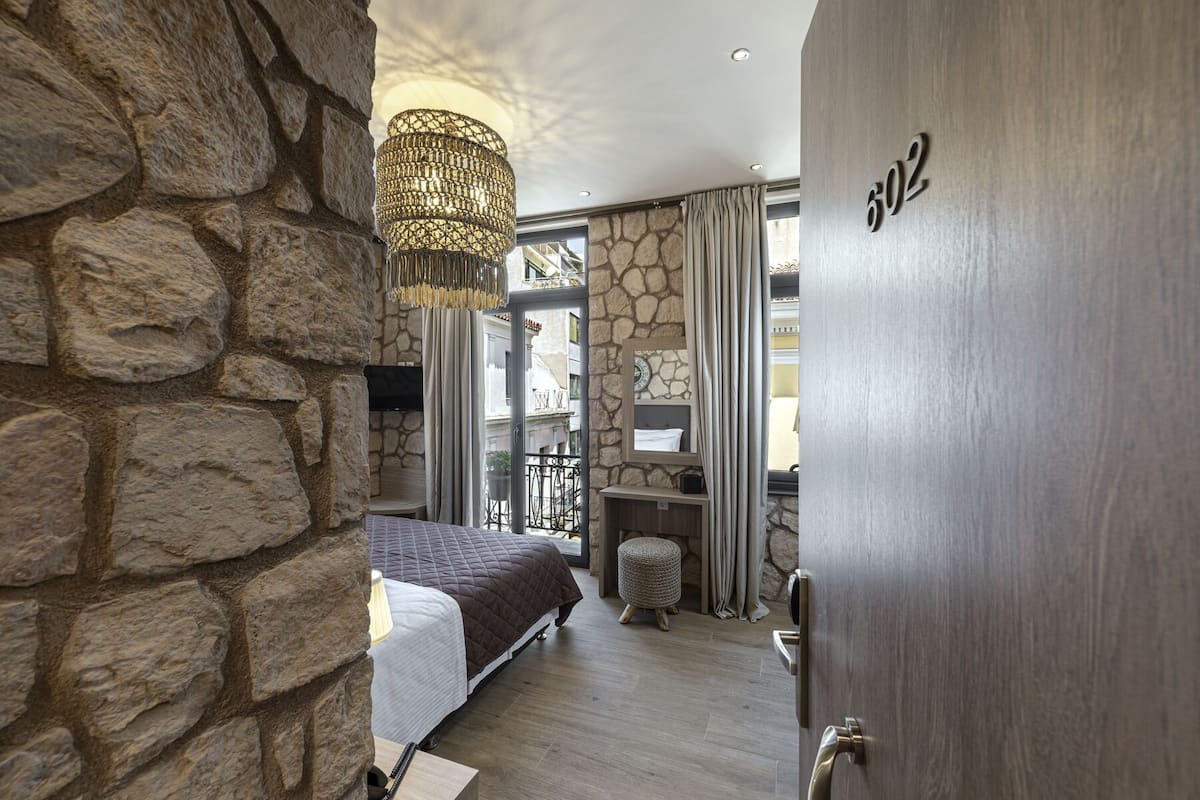 Une chambre avec un mur en pierre, un lit, un luminaire suspendu, une salle de bain avec un miroir et une porte portant le numéro 602.