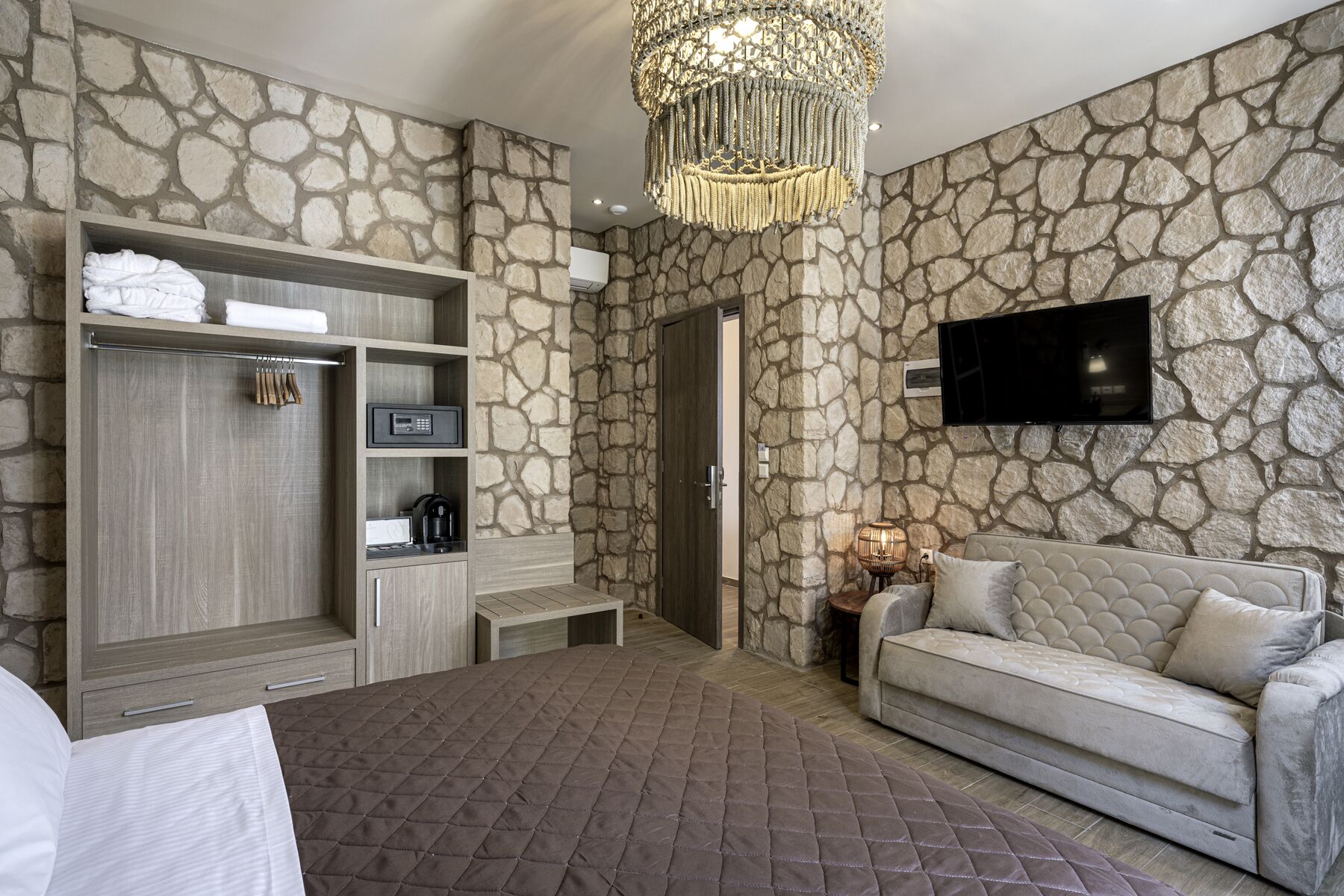Une chambre moderne avec un mur en pierre, un grand lit, un canapé, une télévision et un mini-bar.