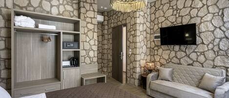 A modern bedroom with a stone wall, a large bed, a sofa, a TV, and a minibar.