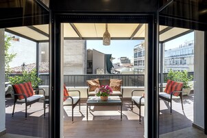 A balcony with wicker furniture, a glass table, and a potted plant.