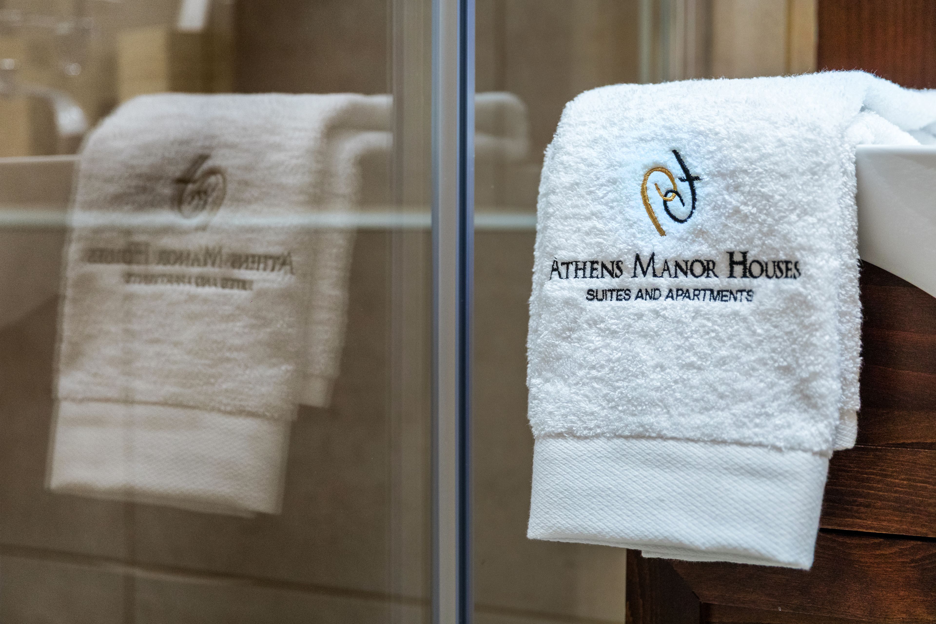 Zwei weiße Handtücher mit Logos und Aufschriften, die darauf hinweisen, dass sie aus dem Athens Manor Houses stammen, einem Hotel mit Suiten und Apartments.