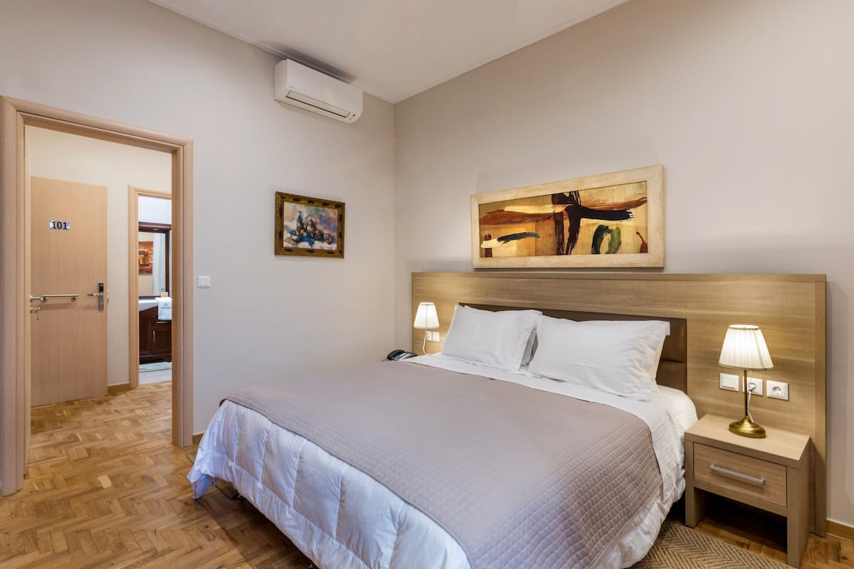 Une chambre d’hôtel bien aménagée, avec un grand lit, des lampes de chevet, une tête de lit en bois, un tableau au mur et une porte portant l’inscription « 101 ».