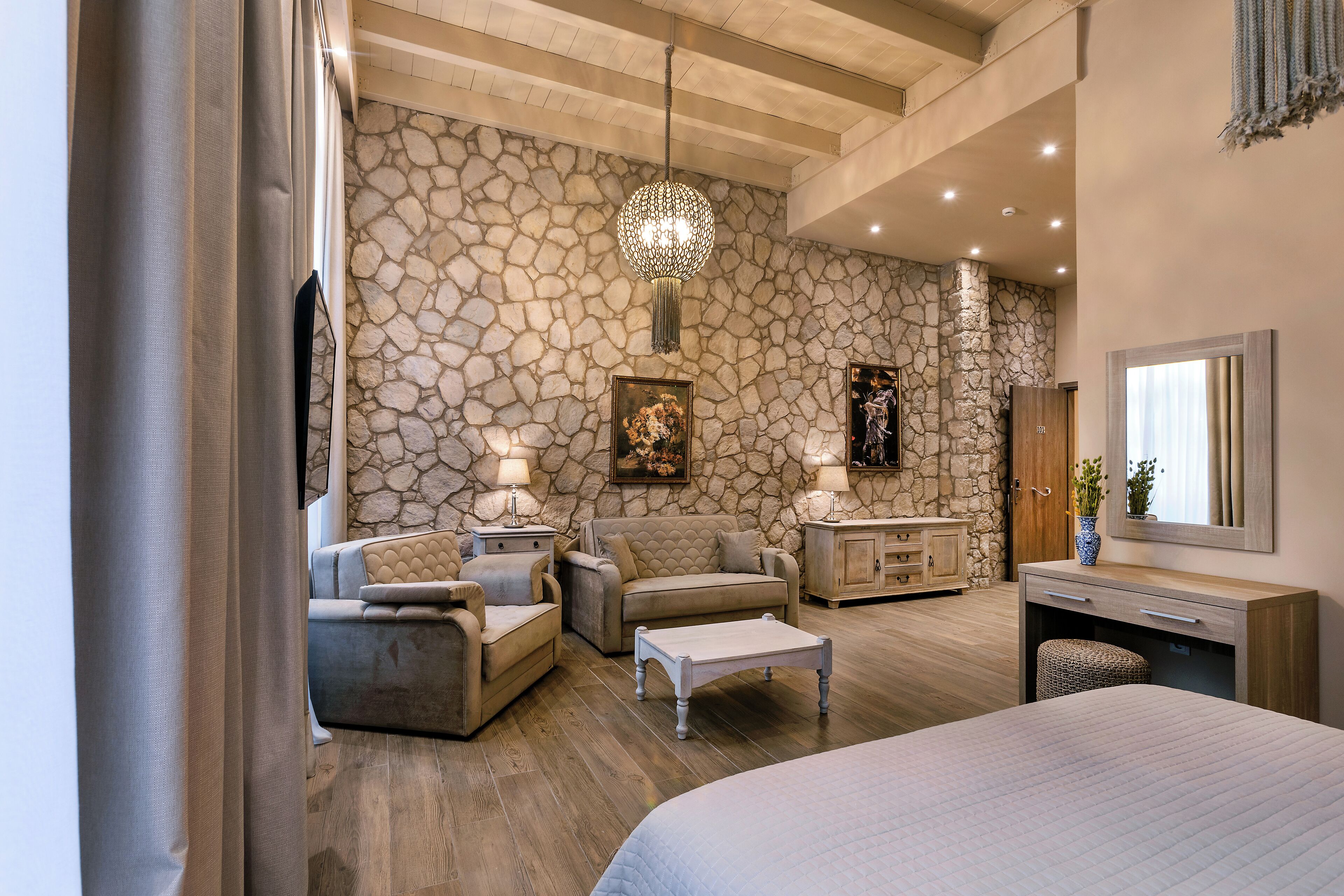 Quarto com parede de pedra, cama, sofá, mesa de centro e cômoda.