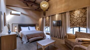 A spacious bedroom with a large bed, a wooden nightstand, a bedside table, a flat-screen TV, a stone accent wall, and a stone fireplace.