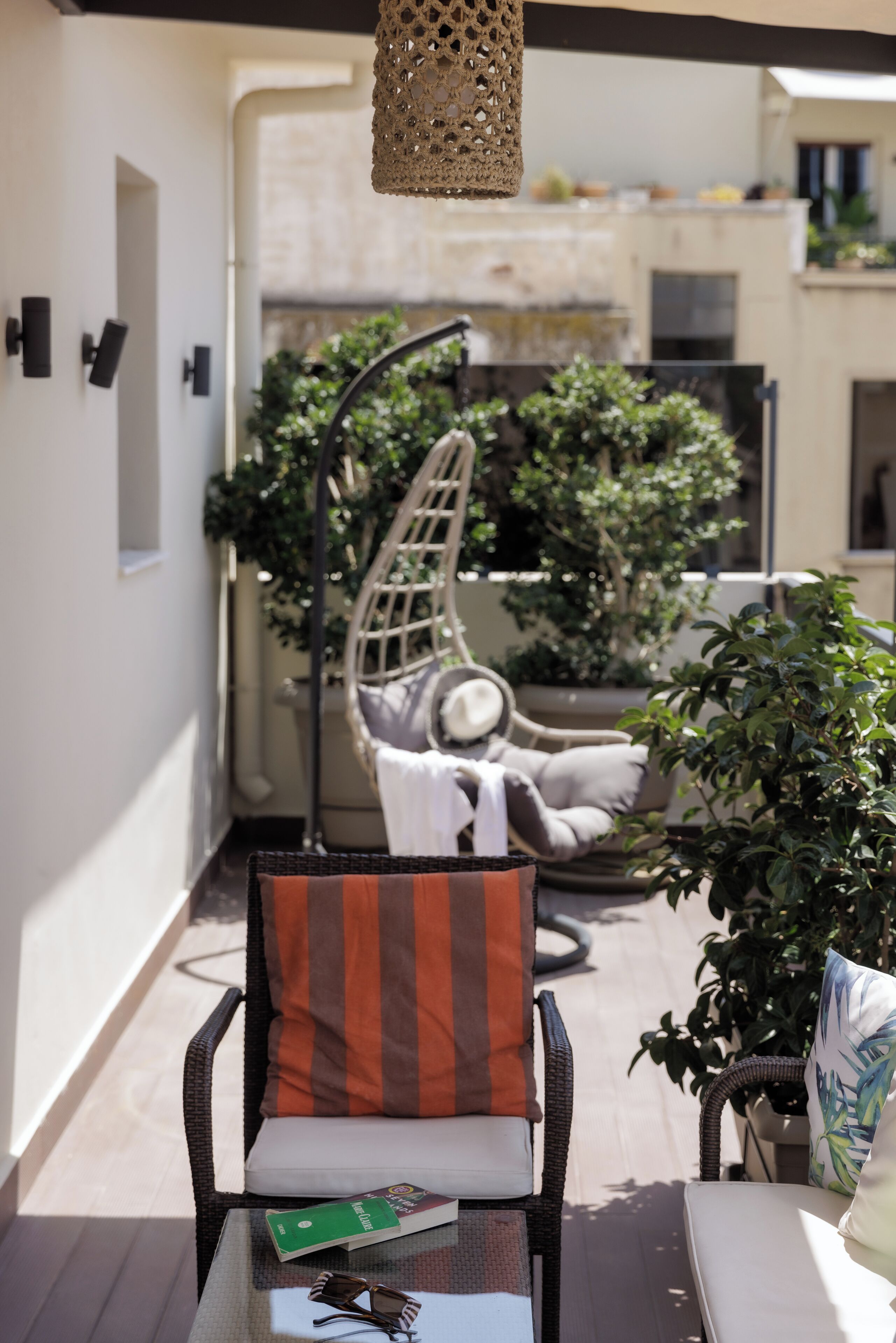A patio with a wicker chair, a cushioned bench, and a hanging light fixture.