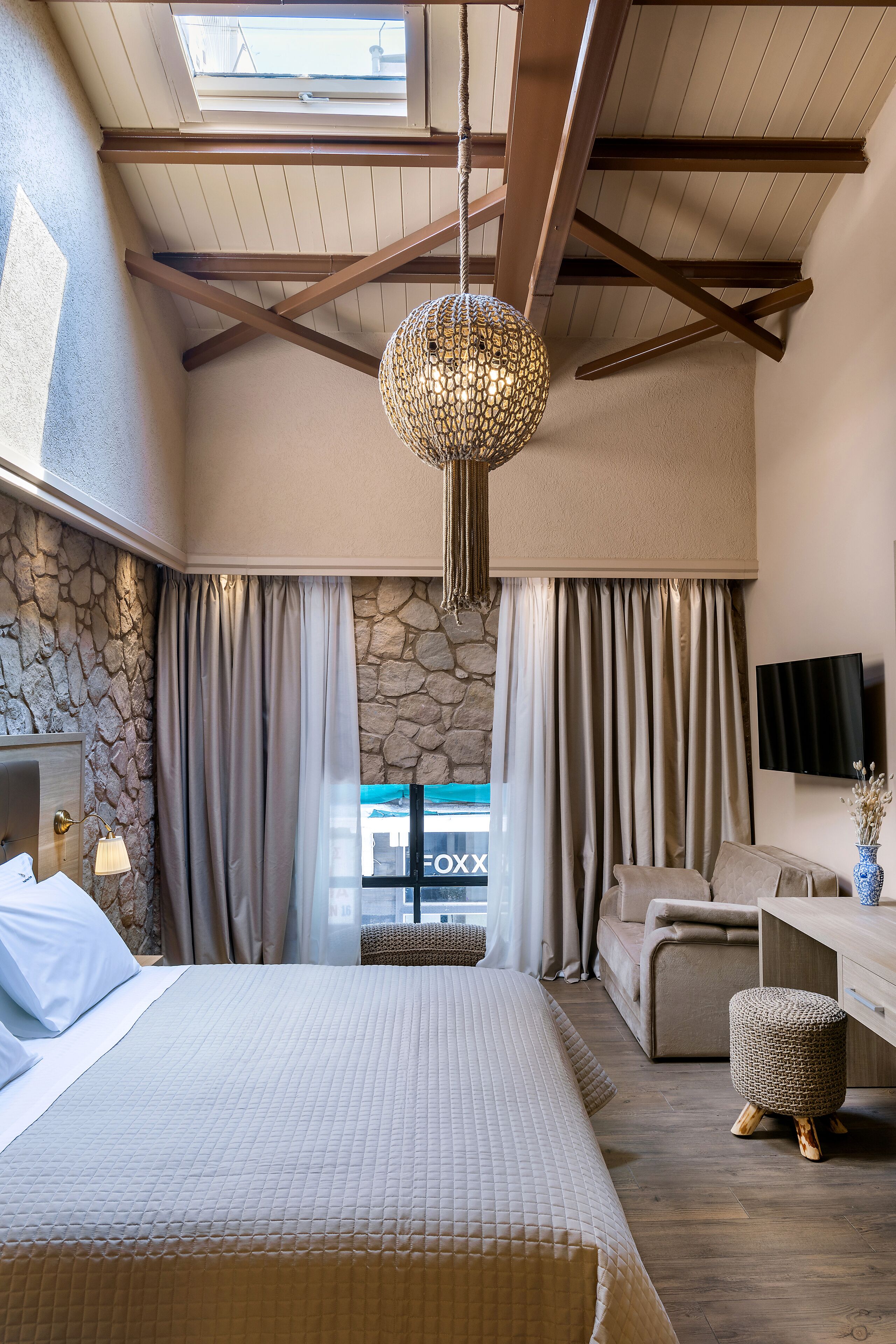 A bedroom with a large bed, a stone wall, a TV, and a desk area.