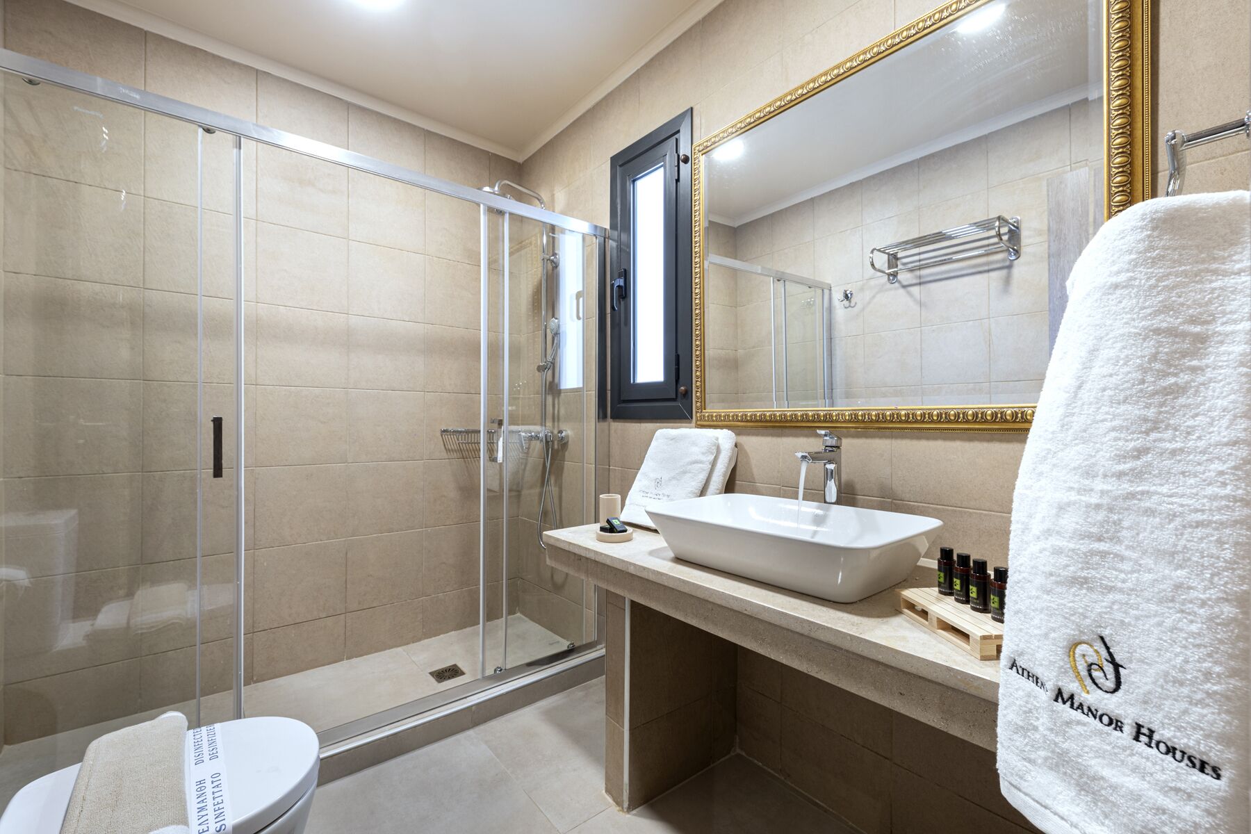 Un bany modern amb dutxa envidrada, un gran mirall amb marc daurat i un lavabo amb poció blanca.