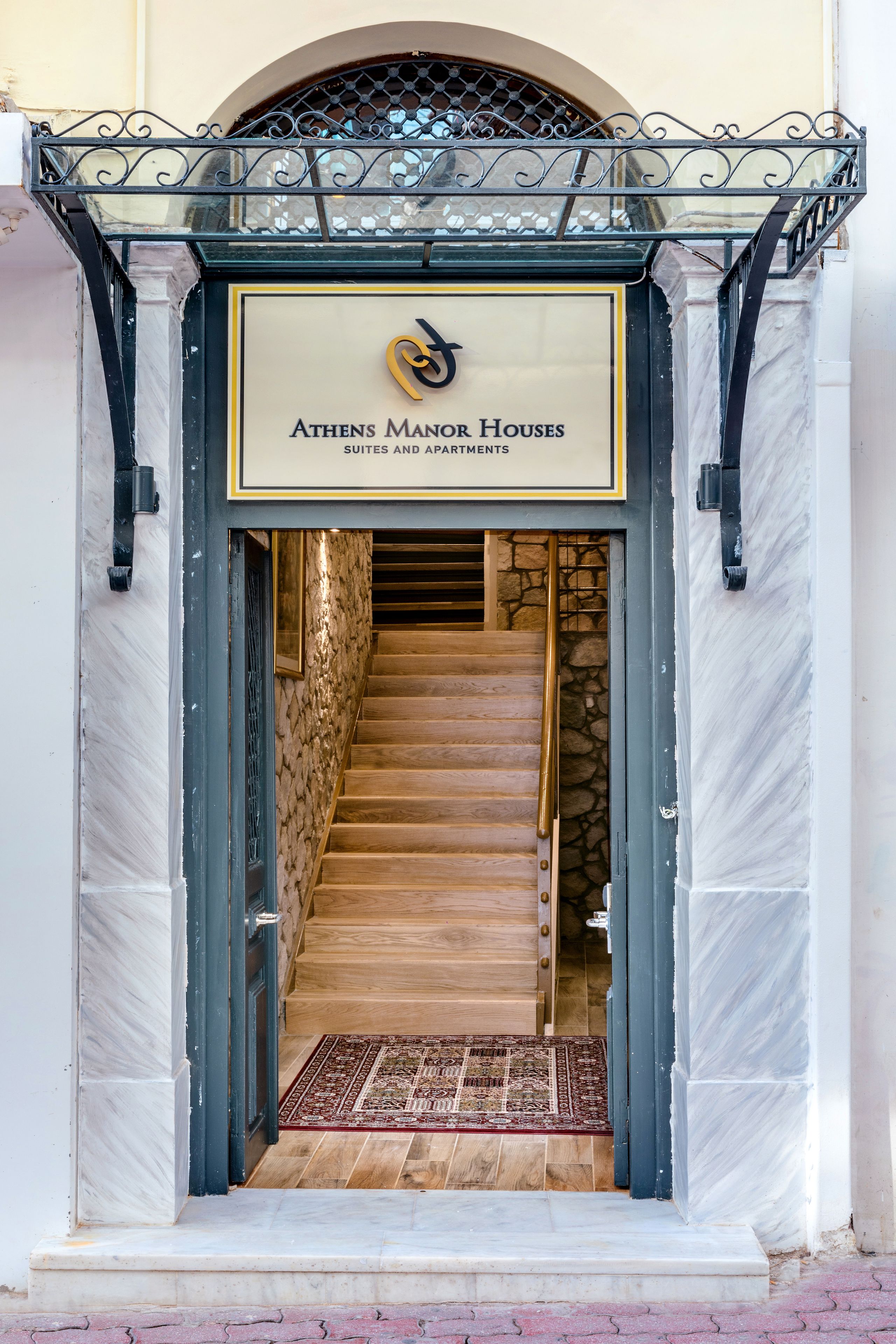 En trappe fører op til en bygningseingang med et skilt, der viser "Athens Manor Houses Suites and Apartments".