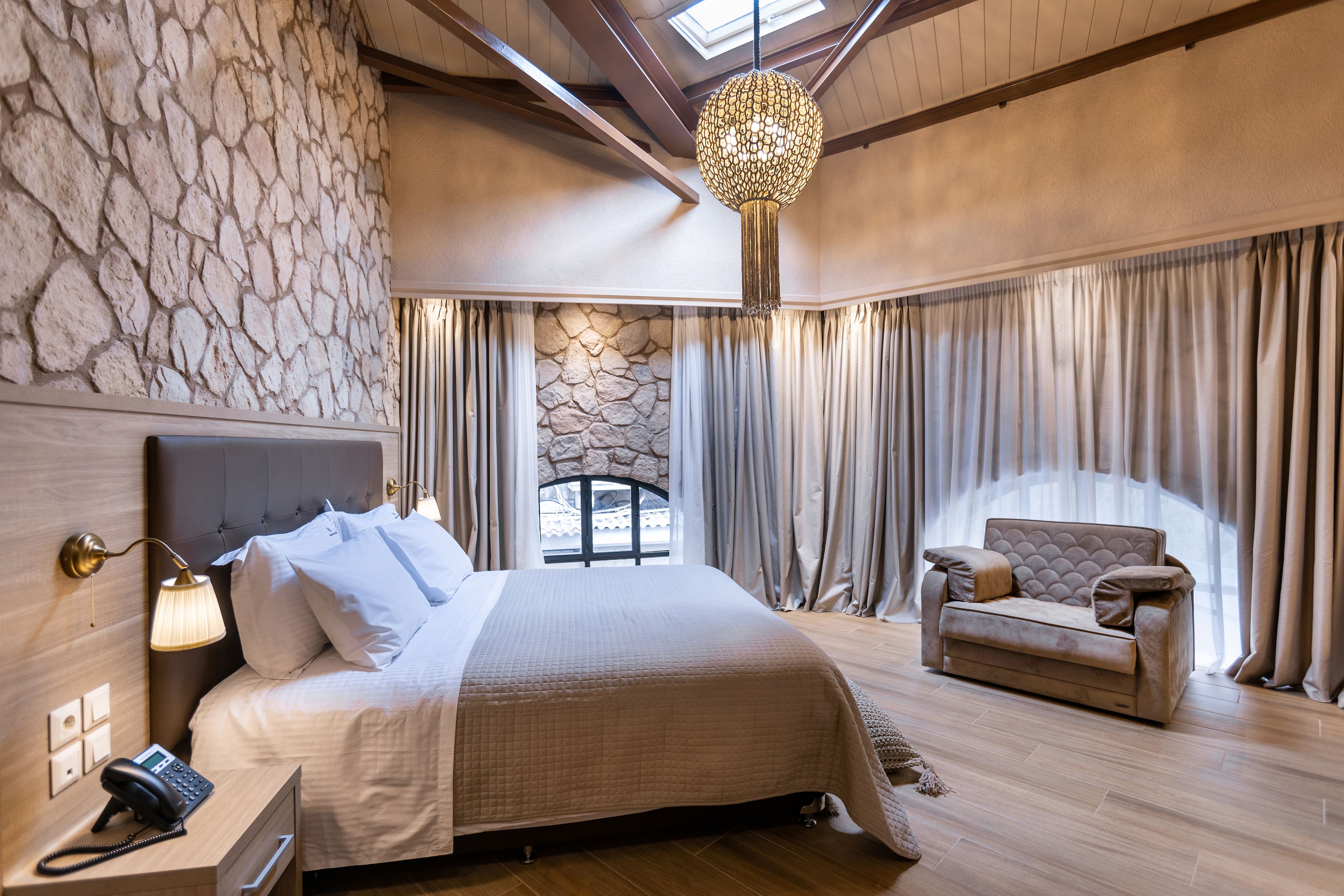 Habitación de hotel con una cama grande, un sofá, una pared de piedra y un tragaluz.