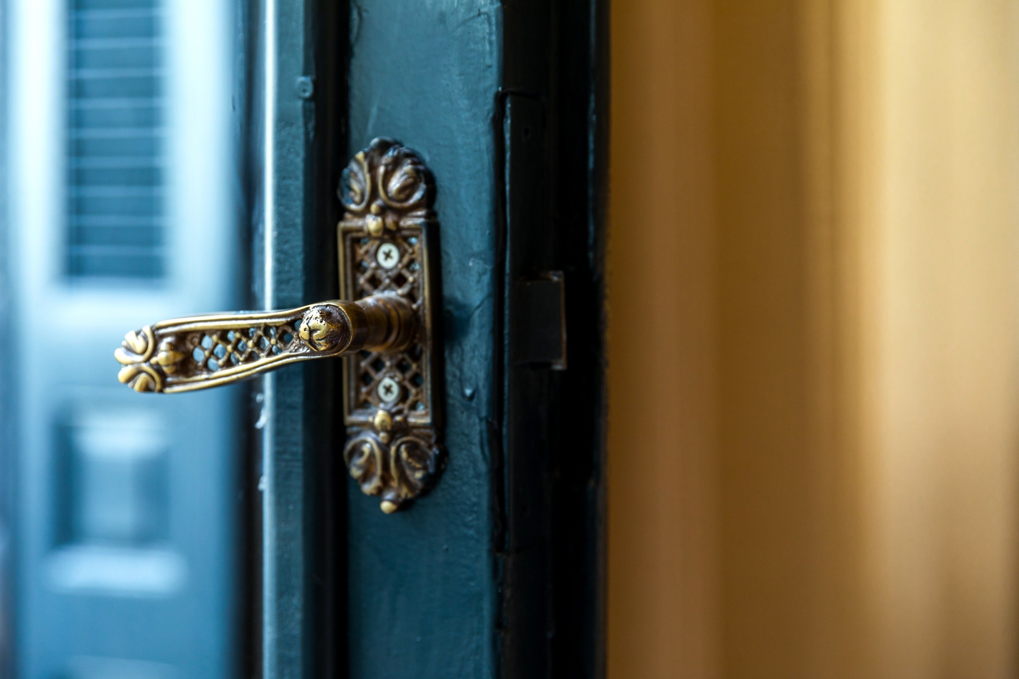 Gros plan sur une poignée de porte en laiton, ornée de motifs complexes, fixée à une porte de couleur sombre.