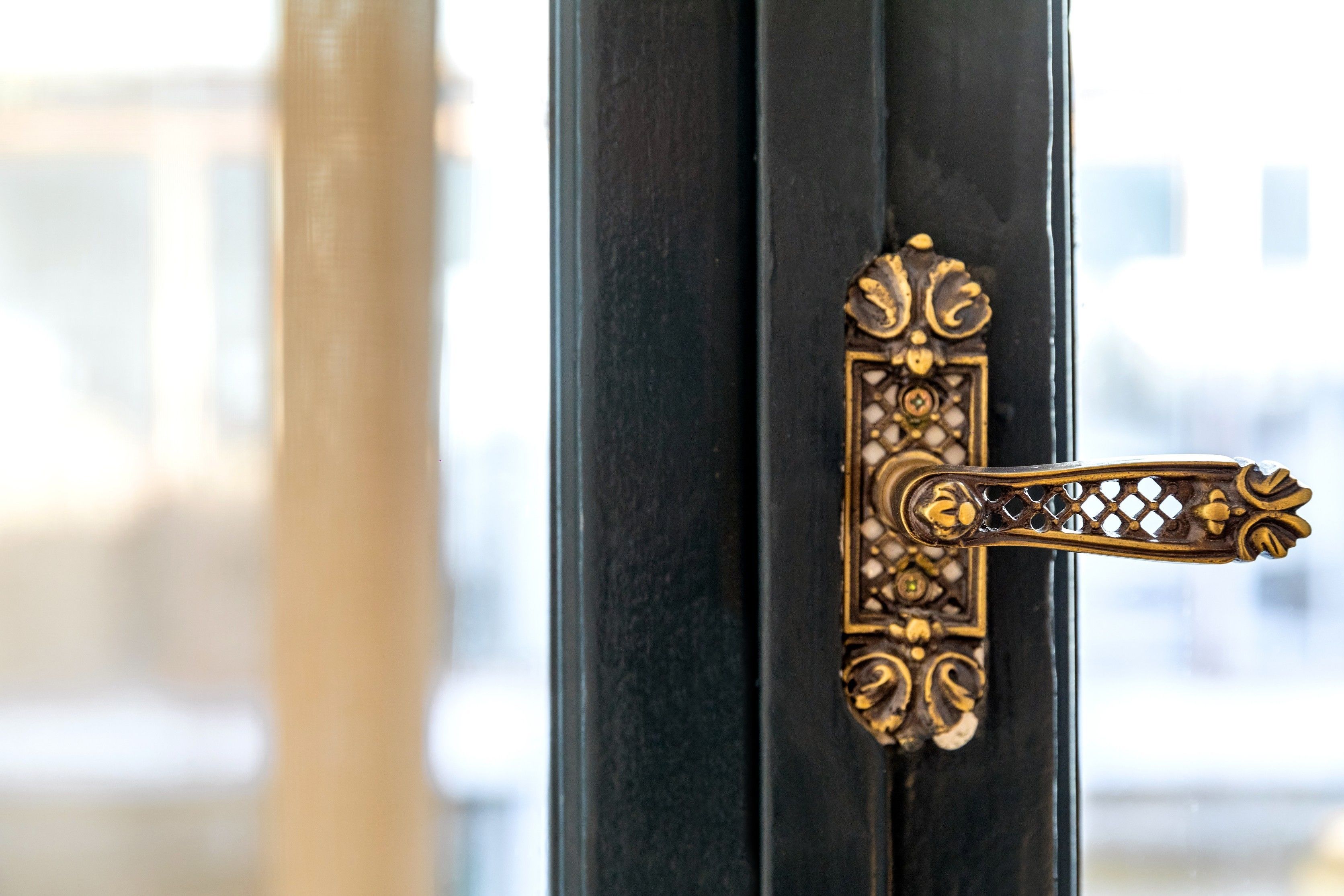 A close-up of a brass door handle with intricate designs, attached to a black door.