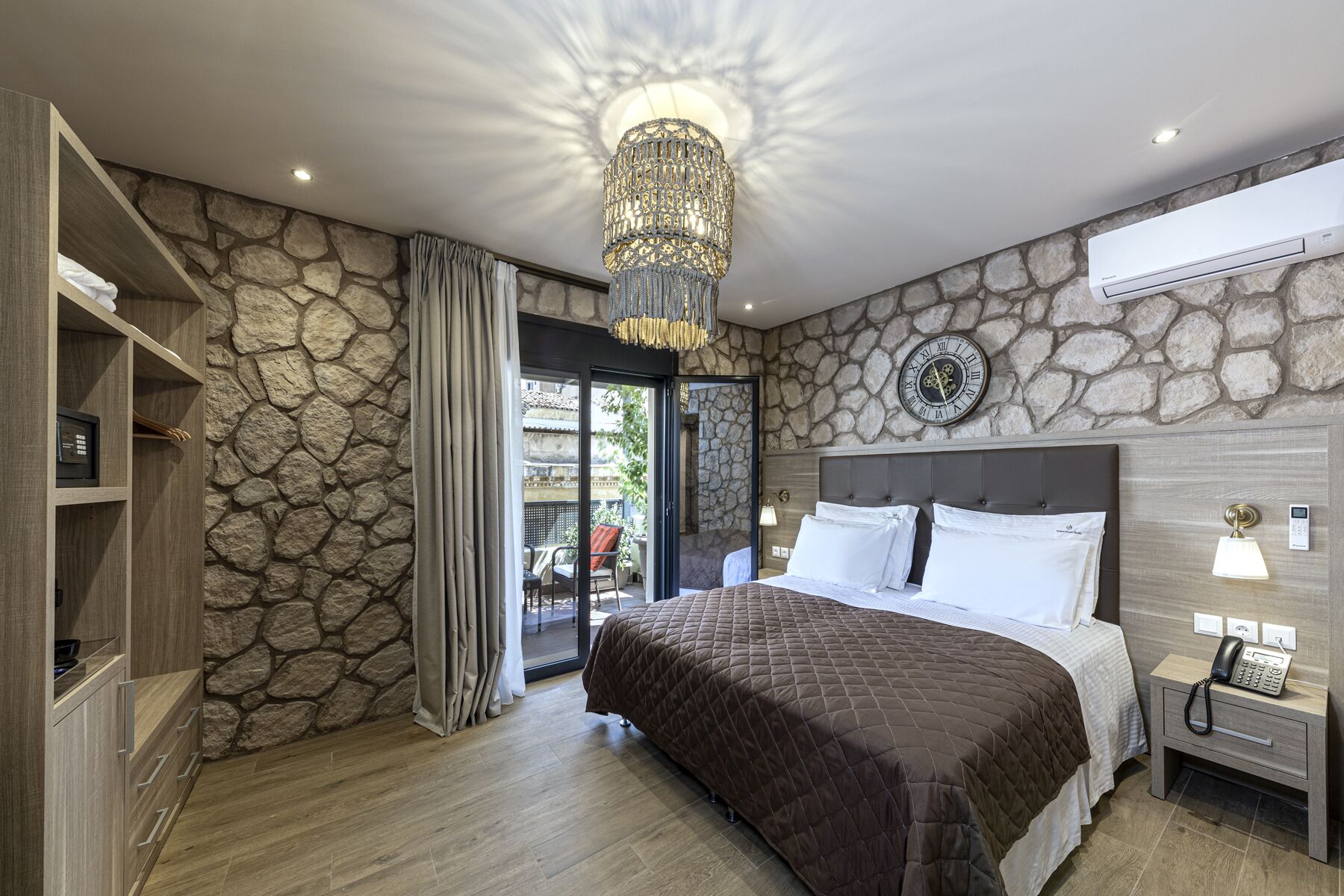 A bedroom with a stone wall, a large bed, a chandelier, and a view through a glass door.