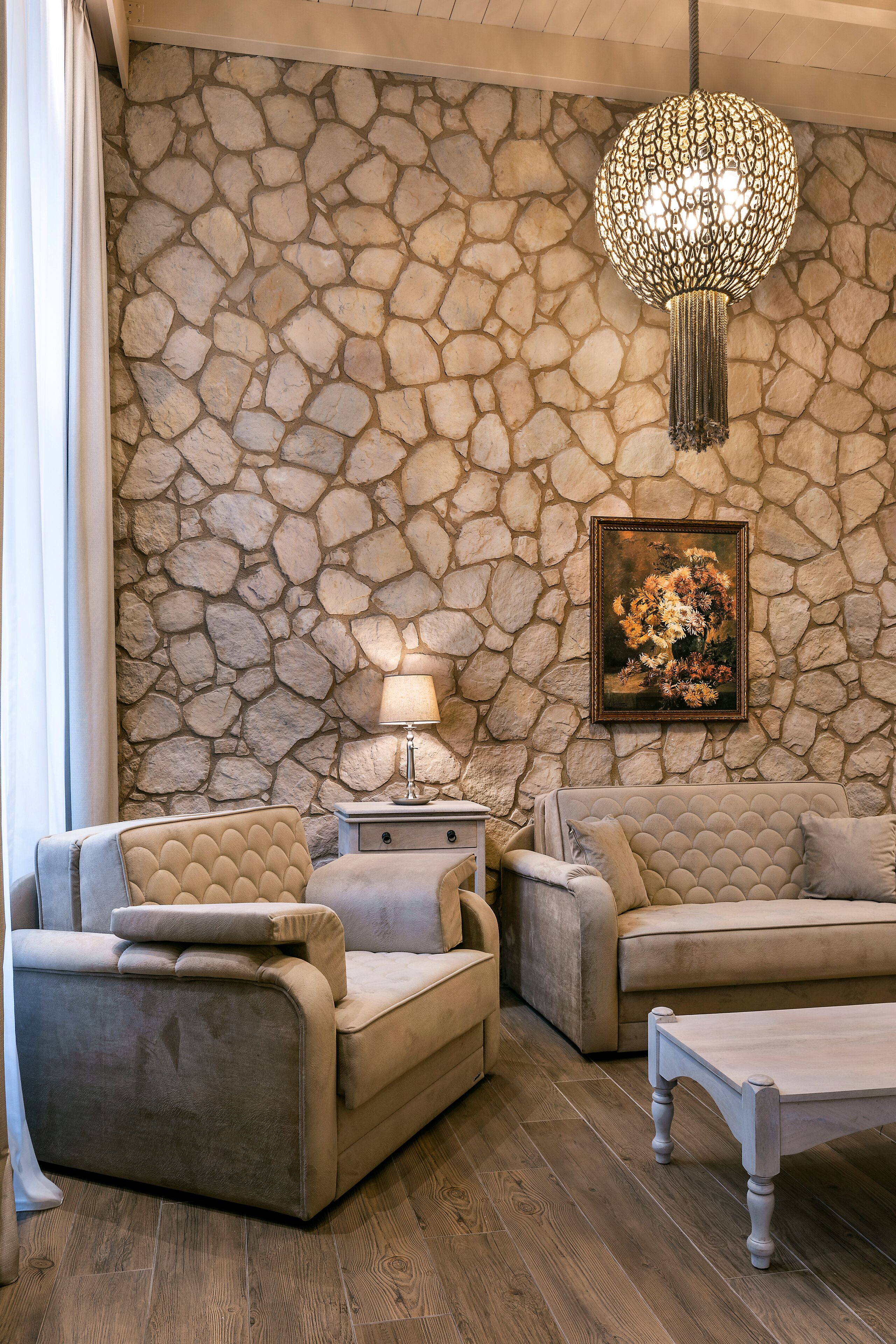 A living room with a stone wall, a chandelier, a painting, and a sofa set.