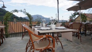 Une terrasse extérieure aménagée avec des meubles en osier, des tables dressées pour les repas et une vue sur les montagnes en arrière-plan.
