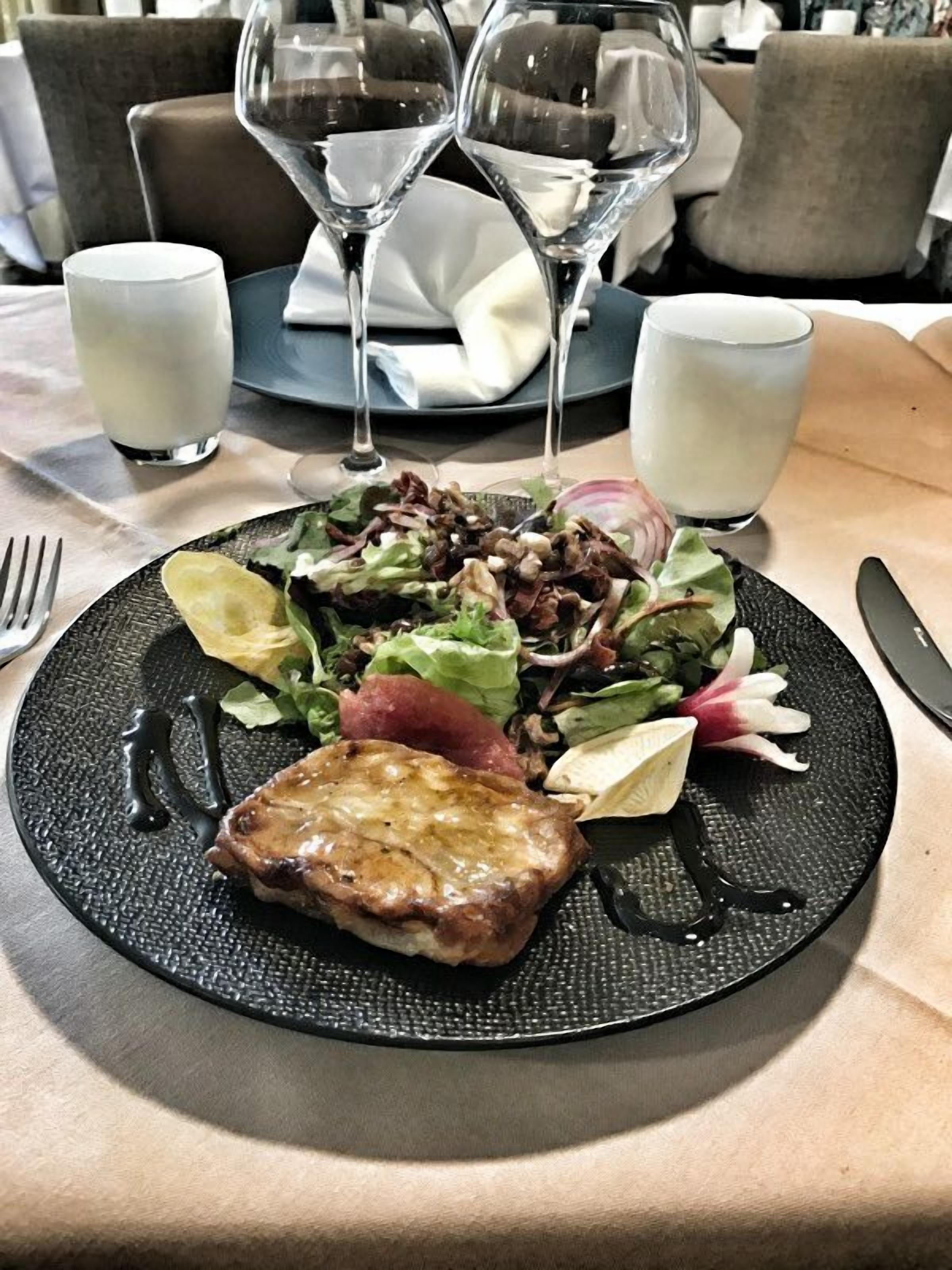 Une assiette avec une salade et un morceau de viande, deux verres d’une boisson claire, ainsi qu’une fourchette et un couteau sur une table.