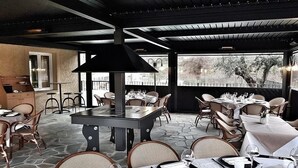 Un espace de restauration en plein air doté d’un sol en pierre, de tables dressées et d’une grande cheminée noire.