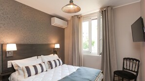 Une chambre d’hôtel avec un grand lit, deux lampes de chevet, un téléviseur fixé au mur et une fenêtre avec des rideaux.