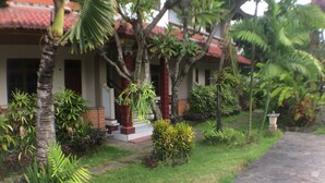 A well-maintained garden with various plants and a stone pathway leading to a building with a red roof. - Mangga Bali Inn (Kuta)