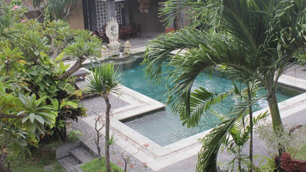 A pool surrounded by tropical plants and a stone pathway. - Mangga Bali Inn (Kuta)