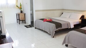A hotel room with two beds, a small table with a plant, and a view of a hallway. - Mangga Bali Inn (Kuta)