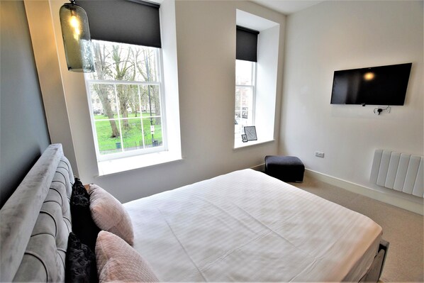 A bedroom with a bed, a window, a TV, and a radiator. - The Hubert - Your Apartment (Bristol)