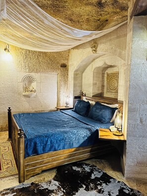 A room with a bed, a nightstand, a lamp, and a cowhide rug. - Caftan Cave Suites (Nevsehir)