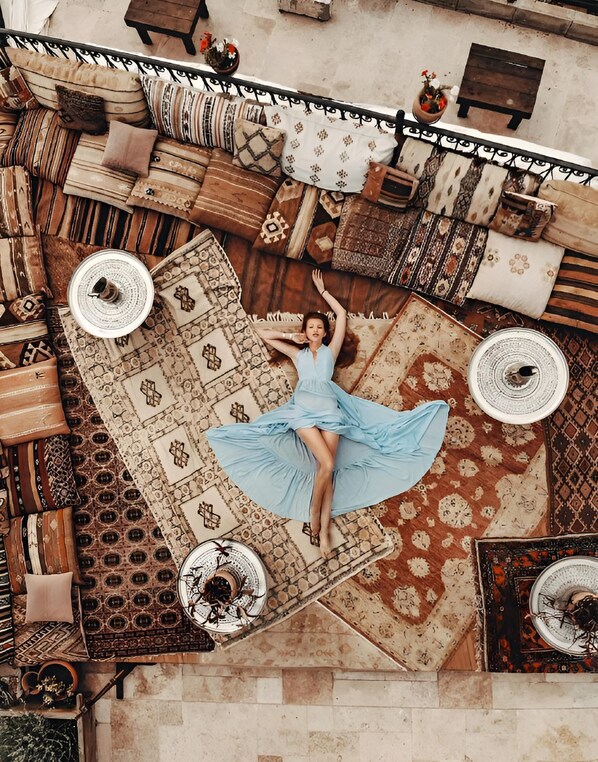 A woman in a blue dress lying on a patterned rug in a room with multiple sofas and a dining table. - Caftan Cave Suites (Nevsehir)