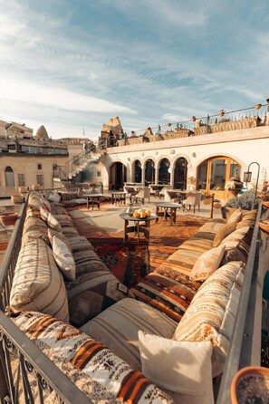 A rooftop terrace with a long sofa, outdoor seating, and a view of the cityscape. - Caftan Cave Suites (Nevsehir)