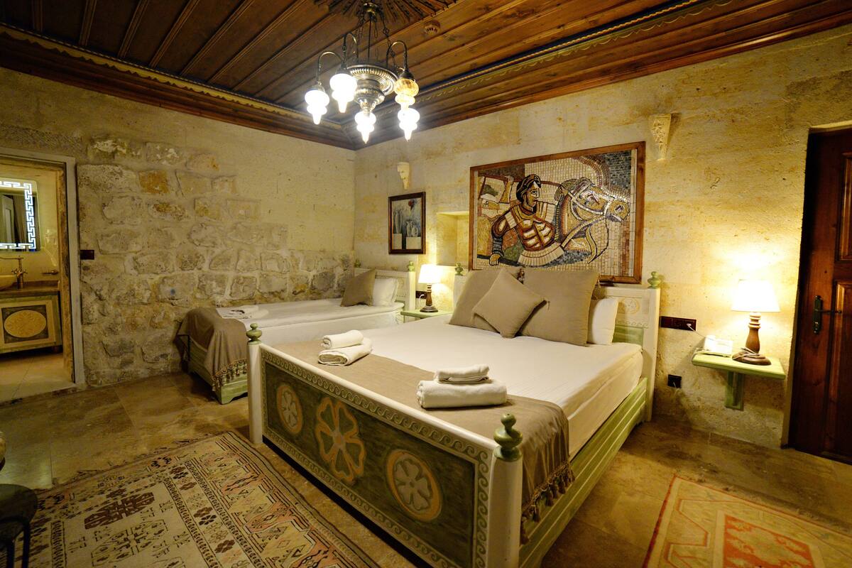 Una habitación tradicional con una cama grande, una mesita de noche pequeña, un espejo y una obra de arte con mosaicos en la pared.