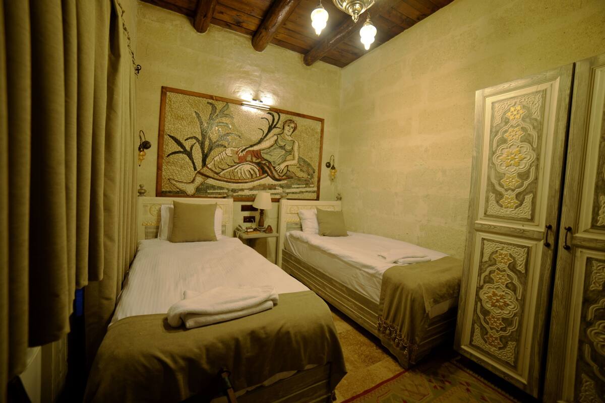 Una habitación con dos camas, un cuadro decorativo grande, un armario y una araña.