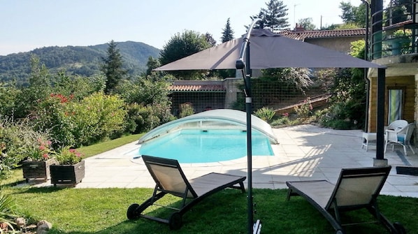 Un jardin avec une piscine, deux chaises longues, une pergola avec un auvent et une vue sur une montagne.