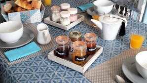 Une table de petit-déjeuner avec des croissants, du jus d’orange et divers condiments, le tout disposé sur une nappe à motifs.
