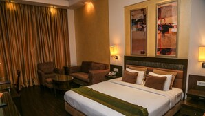 A hotel room with a large bed, a sofa, a chair, a small table, and a desk. - Hotel Western Court (Panchkula)