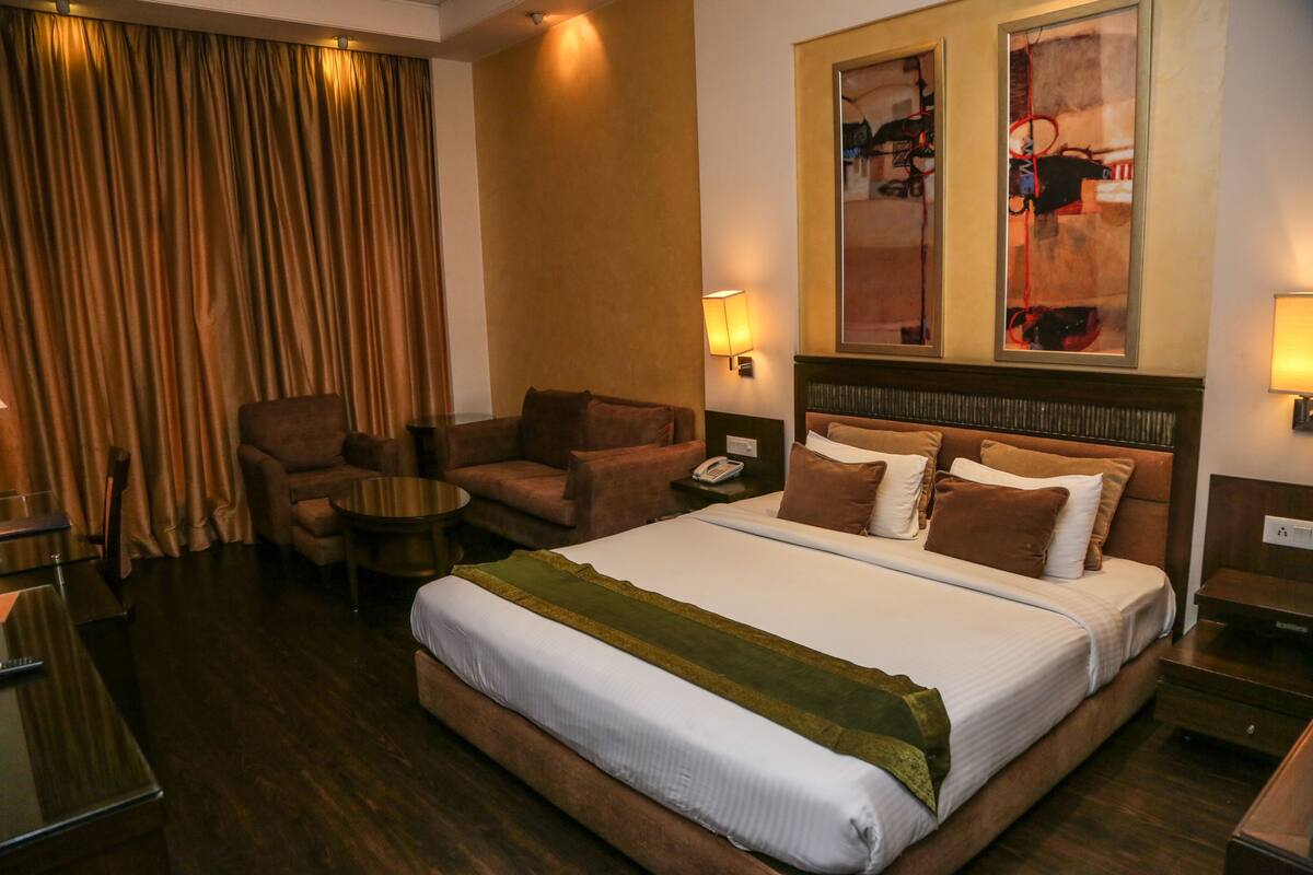 A hotel room with a large bed, a sofa, a chair, a small table, and a desk.
