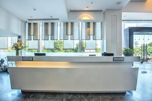A reception desk with a 'CASHIER' and 'RECEPTION' sign, large windows with blinds, and a view of greenery outside. - Hotel Western Court (Panchkula)