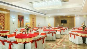 A banquet hall with round tables, white chairs, and red sashes. - Hotel Western Court (Panchkula)