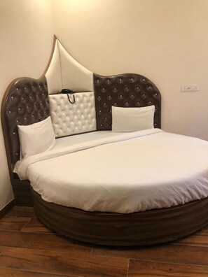 A bed with a round wooden frame, a tufted headboard, and two white pillows. - Hotel Western Court (Panchkula)