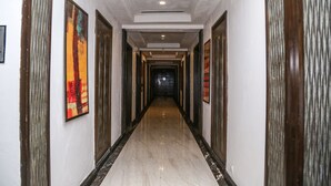 A hallway with a marble floor, framed artwork on the walls, and doors leading to rooms. - Hotel Western Court (Panchkula)