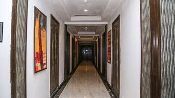A hallway with a marble floor, framed artwork on the walls, and doors leading to rooms.