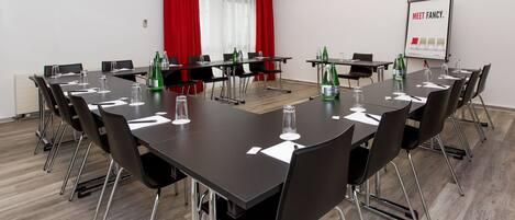 Un salón de conferencias con una pizarra, cortinas rojas y un cartel que dice 'MEET FANCY'.