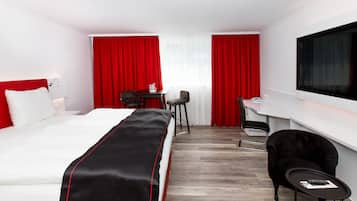Una habitación de hotel con cama, escritorio, silla, televisor y cortinas rojas.