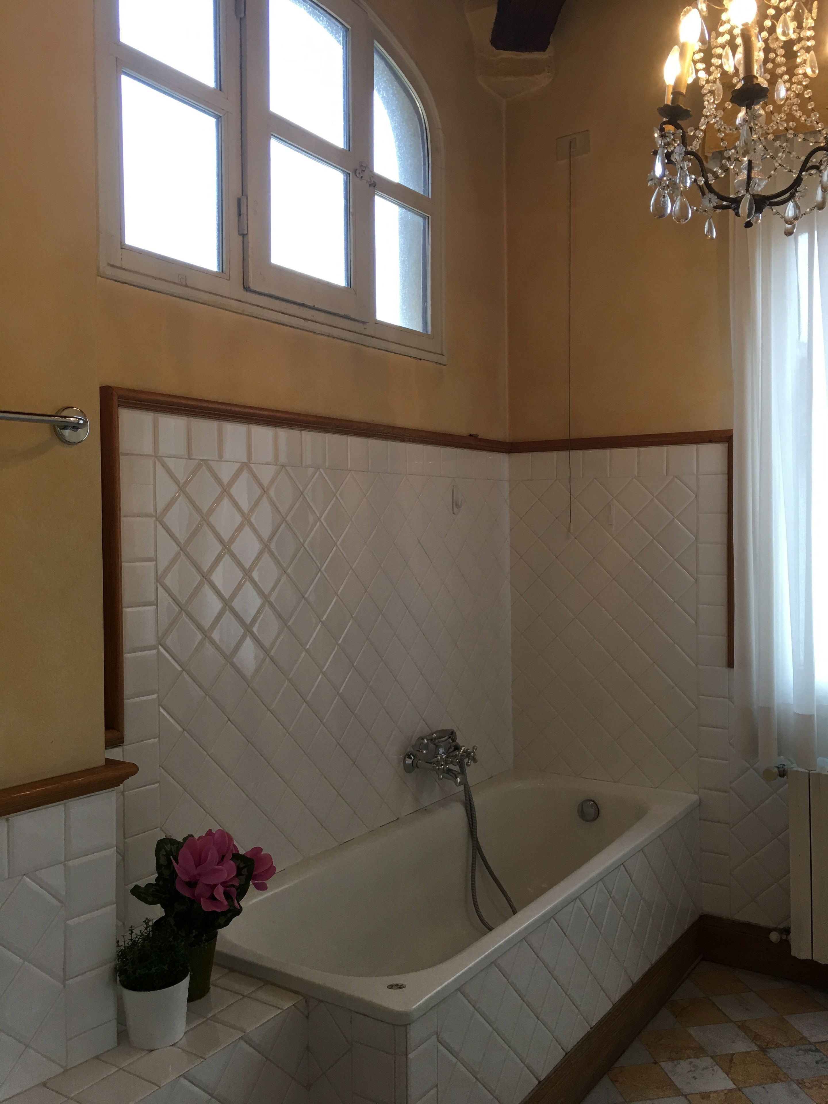 A bathroom with a freestanding bathtub, a window with a view, and a chandelier.