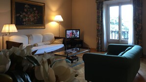 A hotel room with a sofa, a TV, a lamp, a painting, and a window with curtains. - Oriuolo Giotto (Florence)