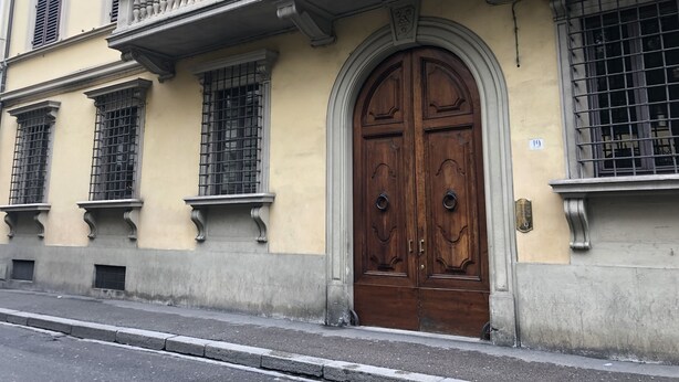 A building facade with a large wooden double door, multiple windows with metal bars, and a balcony with balustrades. - Oriuolo Giotto (Florence)