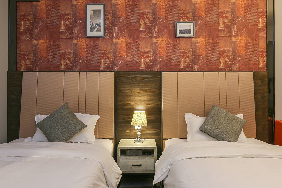 A hotel room with two beds, a nightstand with a lamp, and a wooden headboard.