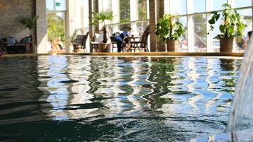 Une piscine intérieure dont l’eau reflète les chaises et les plantes en pot.
